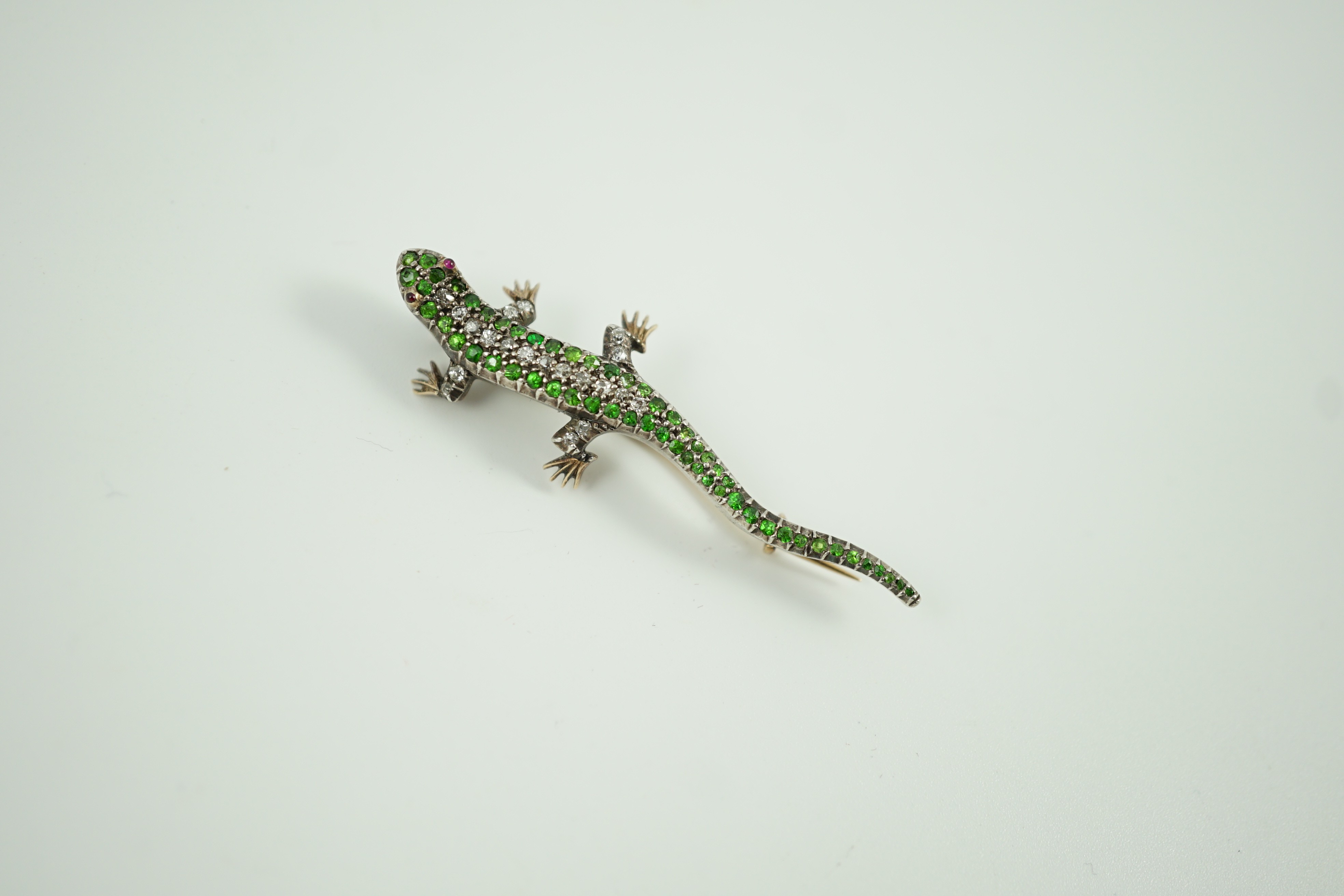 An Edwardian yellow metal, diamond and green garnet set lizard brooch, with red cabochon eyes, 50mm, gross weight 6.2 grams.